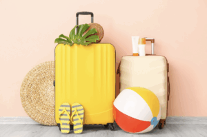 Bright yellow and cream suitcases with summer travel essentials including flip-flops, sunscreen, a beach ball, and a woven hat, perfect for a mindful, recovery-focused vacation.